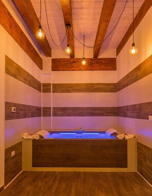 Un spa moderno con techo de madera, una bañera grande y una fuente de agua con luz azul.