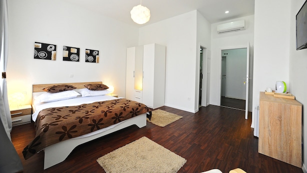 Une chambre à coucher comprenant un lit, des tables de chevet, une armoire, un miroir et un luminaire au plafond.