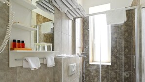 Une salle de bain moderne équipée d’un lavabo, de toilettes et d’une douche. On y trouve également un miroir, un porte-serviettes et une fenêtre qui laisse entrer la lumière naturelle.