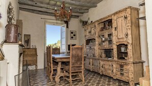 A rustic kitchen with a wooden table and chairs, a chandelier, and a large wooden cabinet with glass doors. - Chambre D'Hôtes La Marlotte (Castello-di-Rostino)