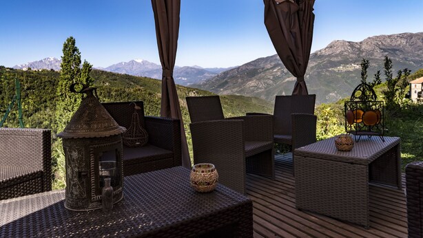 An outdoor seating area with wicker furniture, a decorative lantern, and a view of mountains. - Chambre D'Hôtes La Marlotte (Castello-di-Rostino)