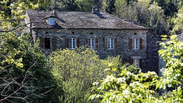 A stone building with multiple windows and a chimney, surrounded by dense forest. - Chambre D'Hôtes La Marlotte (Castello-di-Rostino)