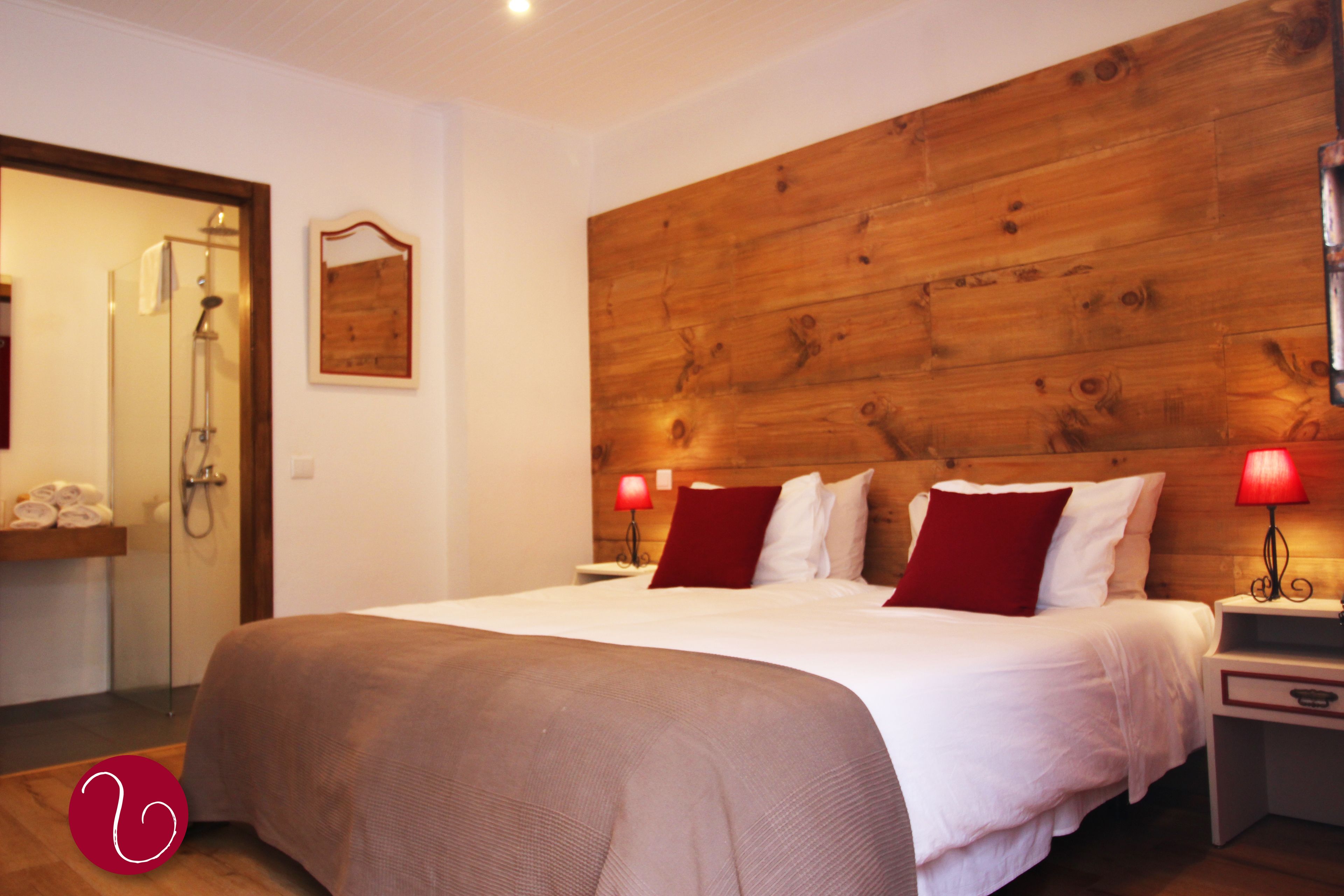 A hotel room with a large bed, wooden headboard, two bedside tables with lamps, a wooden wall panel, a shower area, and a towel rack.