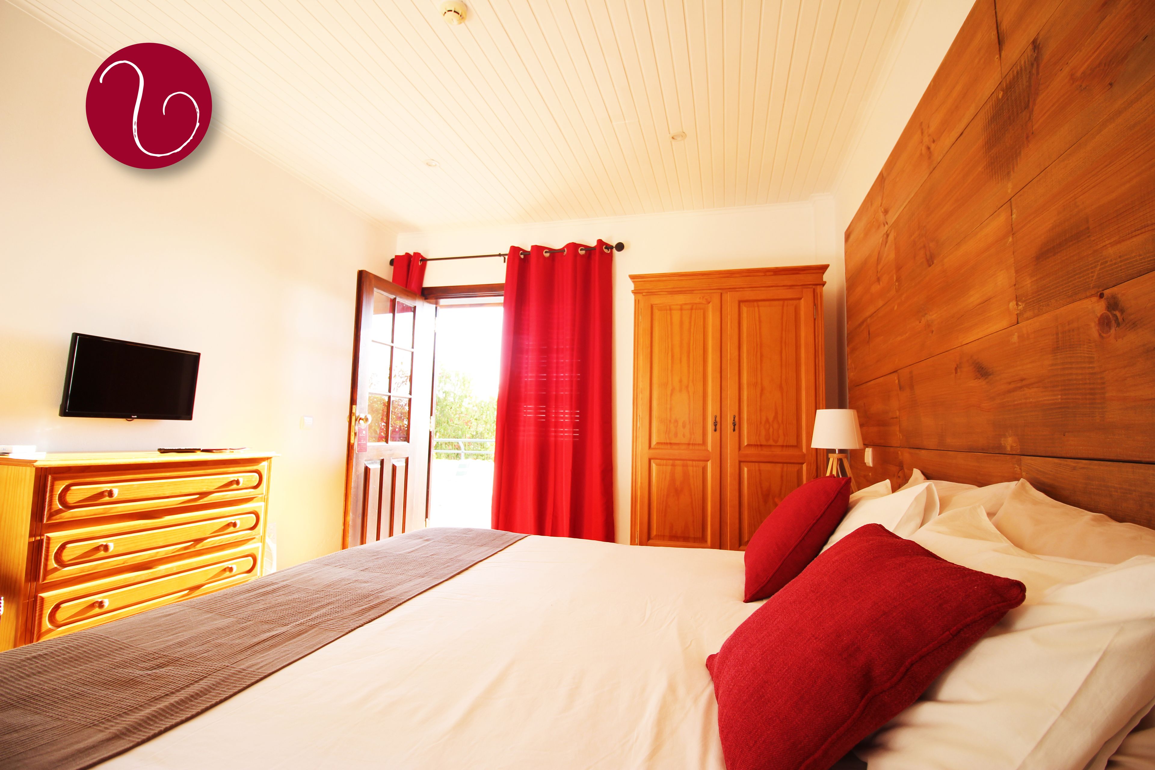A bedroom with a bed, wooden dresser, TV, and a wooden wardrobe.