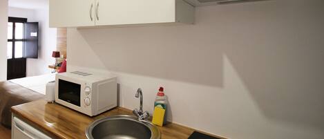 Una cocina compacta con gabinetes blancos, microondas, pileta y lavavajillas.