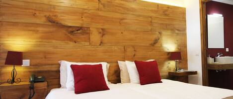 A hotel room with a wooden headboard, a bed with white and red pillows, a bedside table with a lamp, and a bathroom with a mirror and sink.