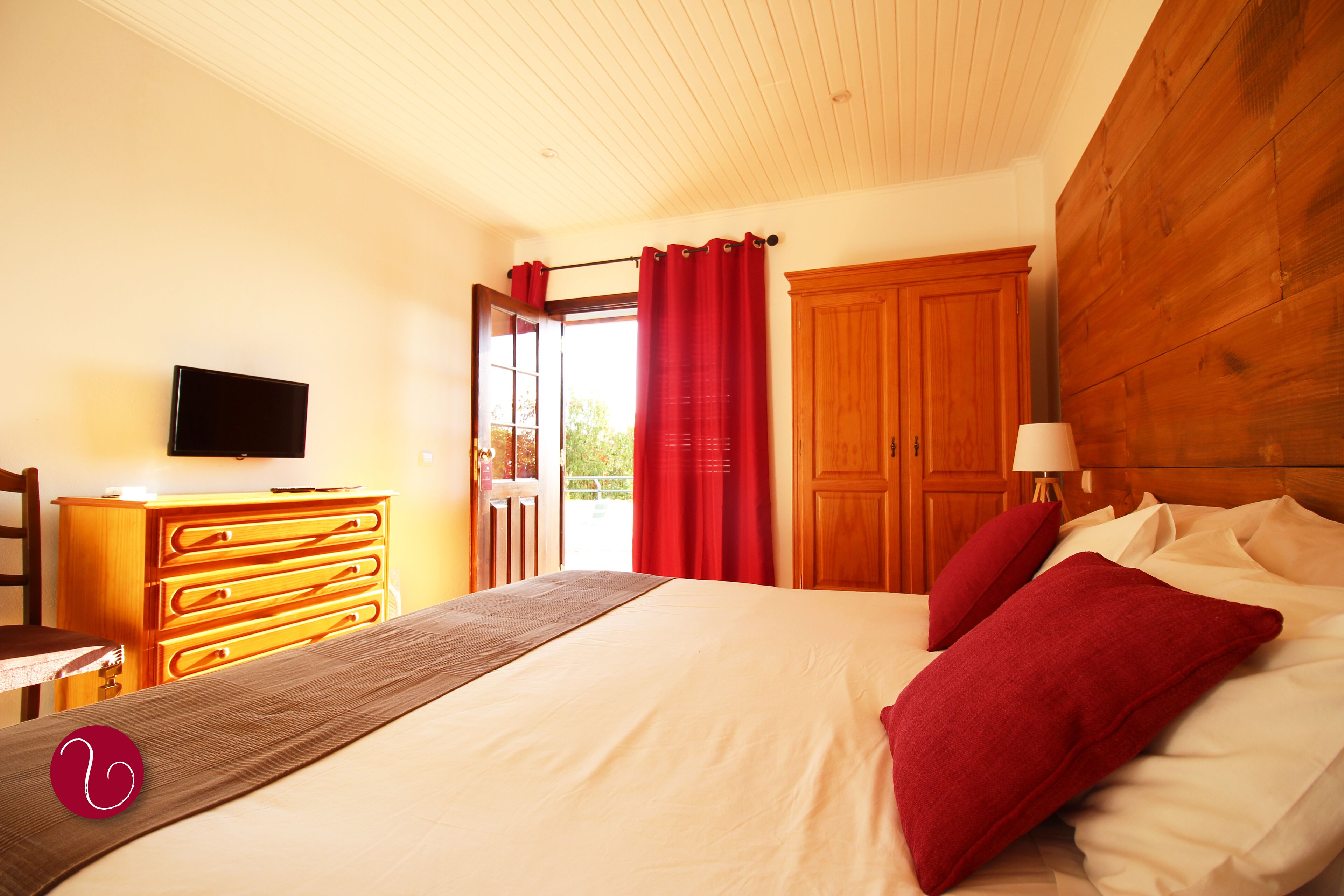 A bedroom with a bed, wooden dresser, TV, and a view of the outdoors.