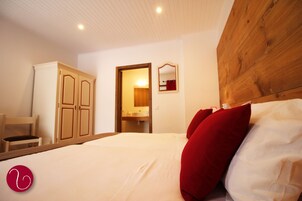 A bedroom with a wooden headboard, a bed with white and red bedding, a wooden wardrobe, and a mirror on the wall.