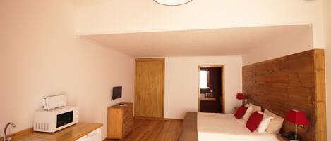 Una habitación compacta con cama de madera, lámparas de noche y una pequeña kitchenette con microondas.