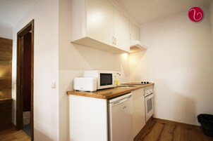Cocina compacta con armarios blancos, microondas, tostadora, fregadero y lavavajillas.