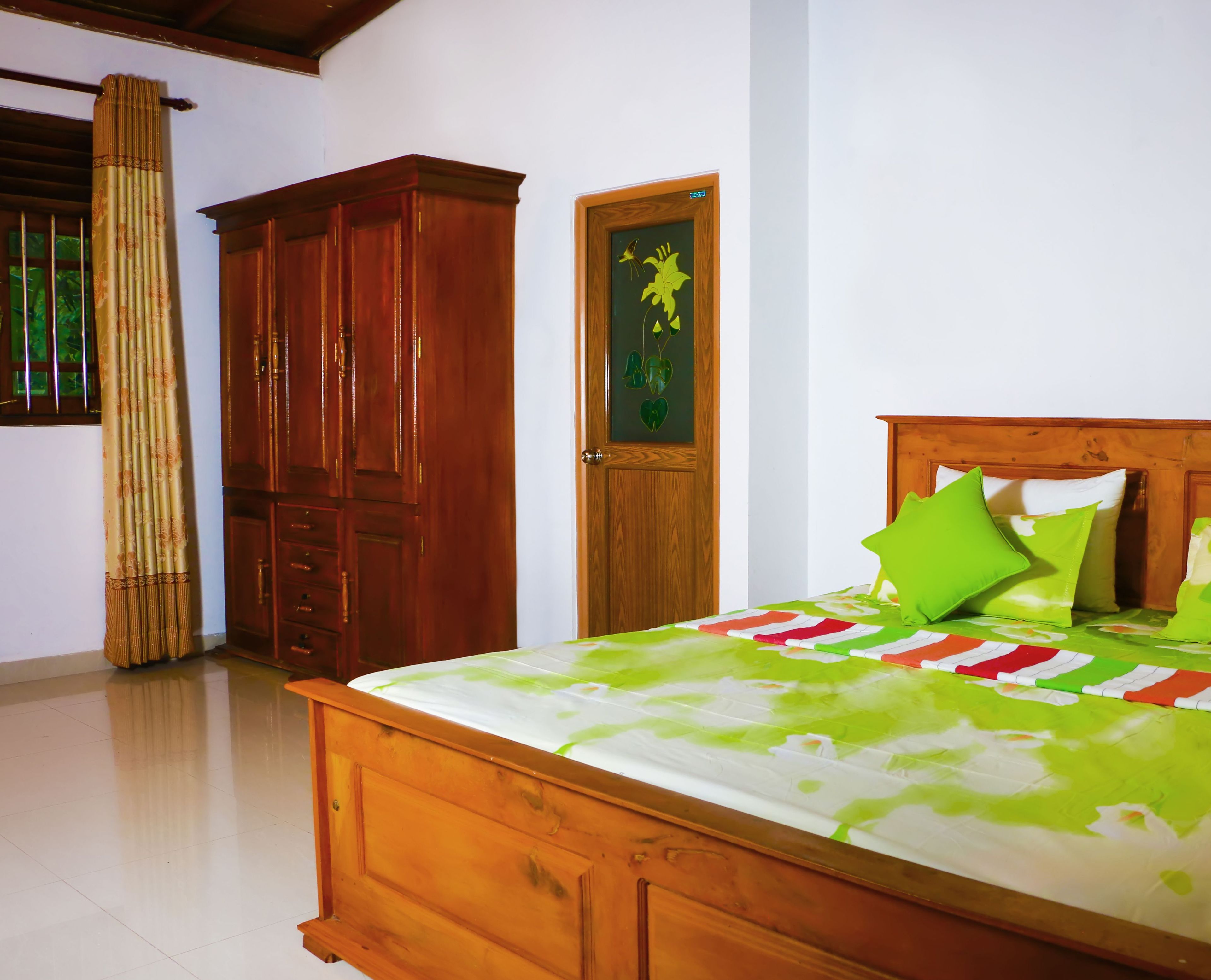 Un dormitorio con cama de madera, colcha floral verde y blanca, y almohada verde.