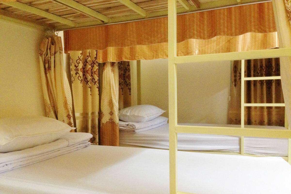 A bunk bed room with a wooden frame, white bedding, and patterned curtains.