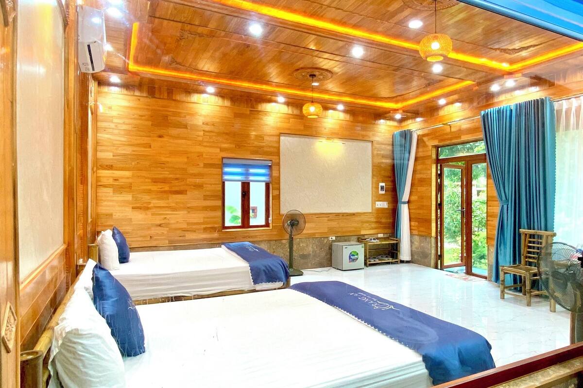 A room with two beds, a fan, a small table, and a window with curtains.