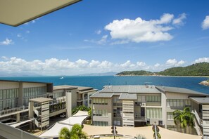 A modern hotel with multiple floors, outdoor terraces, and a view of the sea and distant hills.
