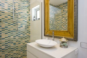 A bathroom with a mosaic tile wall, a white sink, and a large mirror with a decorative frame.