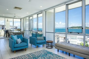 A spacious living room with large windows, two blue armchairs, a beige sofa, and a small round table. - 1 Bright Point Apartment 1504 (Nelly Bay)