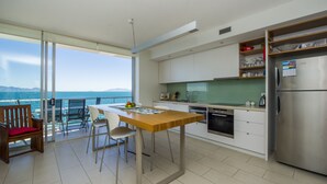 A modern kitchen with a large island, a dining area with a view of the sea, and a balcony with a wooden chair. - 1 Bright Point Apartment 5102 (Nelly Bay)