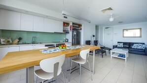 A modern kitchen with white cabinets, a wooden dining table, and a refrigerator. - 1 Bright Point Apartment 5102 (Nelly Bay)