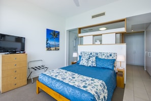 A bedroom with a bed, a TV on a dresser, a painting, and a bathroom with a shower.