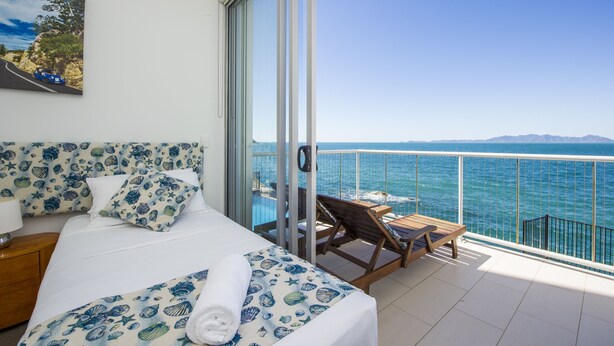 A hotel room with a bed, a small table, a chair, and a balcony with a view of the sea. - 1 Bright Point Apartment 5102 (Nelly Bay)