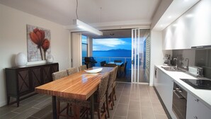A modern kitchen with a dining area, a view through a glass door, and a painting on the wall. - 1 Bright Point Apartment 5201 (Nelly Bay)