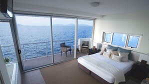A bedroom with a large bed, a balcony with a view of the sea, and a chair. - 1 Bright Point Apartment 5201 (Nelly Bay)