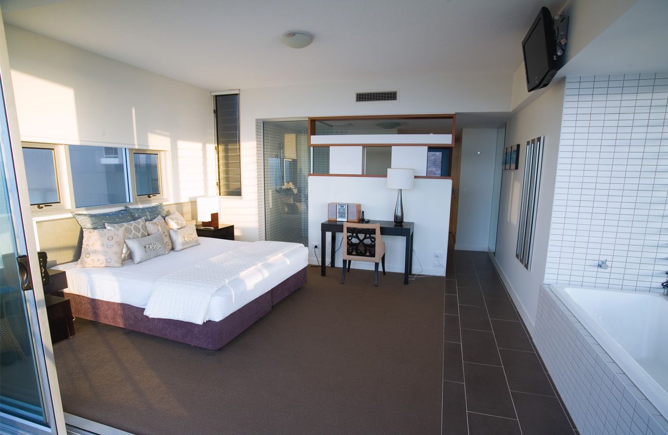 Ein modernes Hotelzimmer mit einem großen Bett, einem Schreibtisch, einem Sessel, einem Fernseher und einem Badezimmer mit Badewanne.