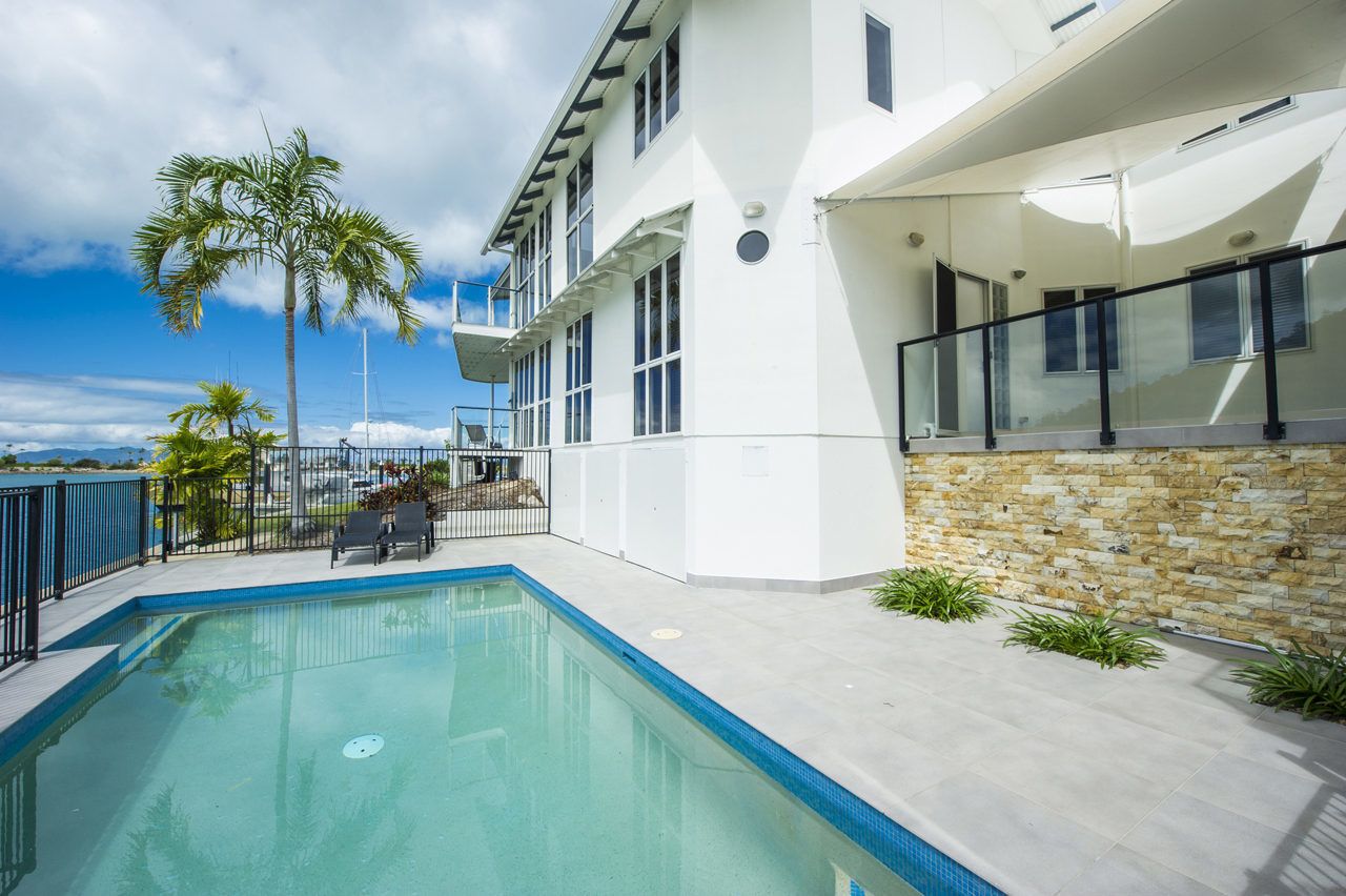 A modern building with a swimming pool, palm trees, and a stone wall.