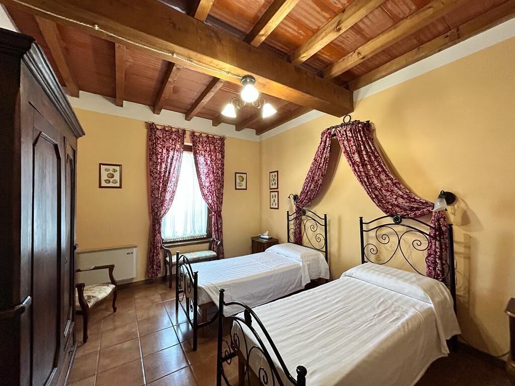 Un dormitorio con dos camas, vigas de madera en el techo, un radiador y una ventana con cortinas.