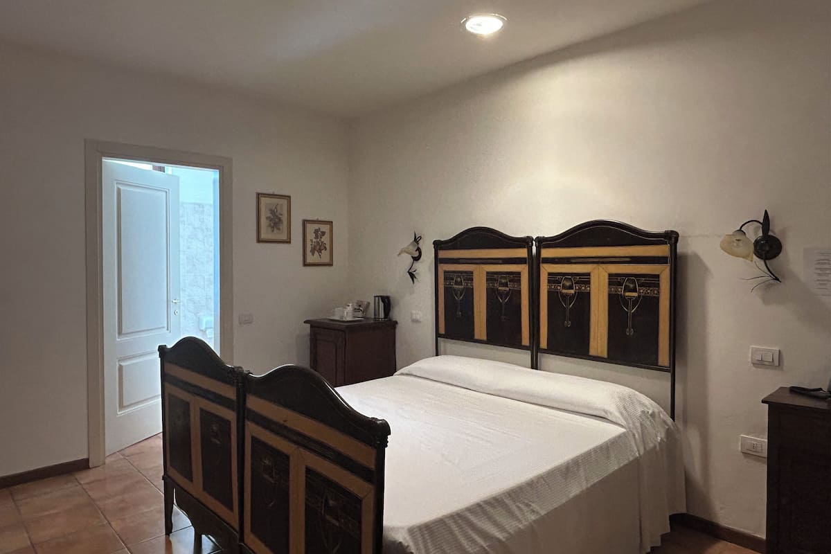 A bedroom with a double bed, a nightstand, a wall-mounted lamp, and a door leading to another room.