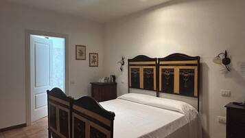 Une chambre à coucher avec un lit double, une table de chevet, une lampe fixée au mur et une porte donnant sur une autre pièce.
