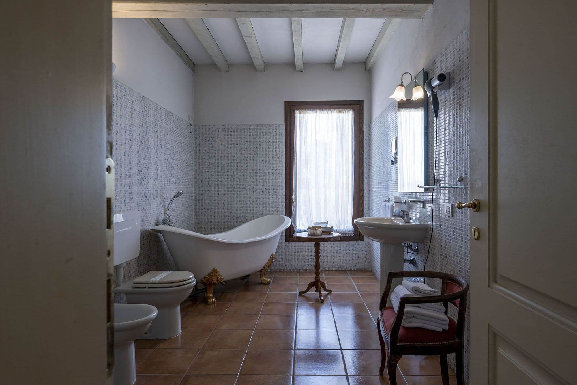 Un baño con una bañera independiente, inodoro, lavamanos y ventana con cortinas.