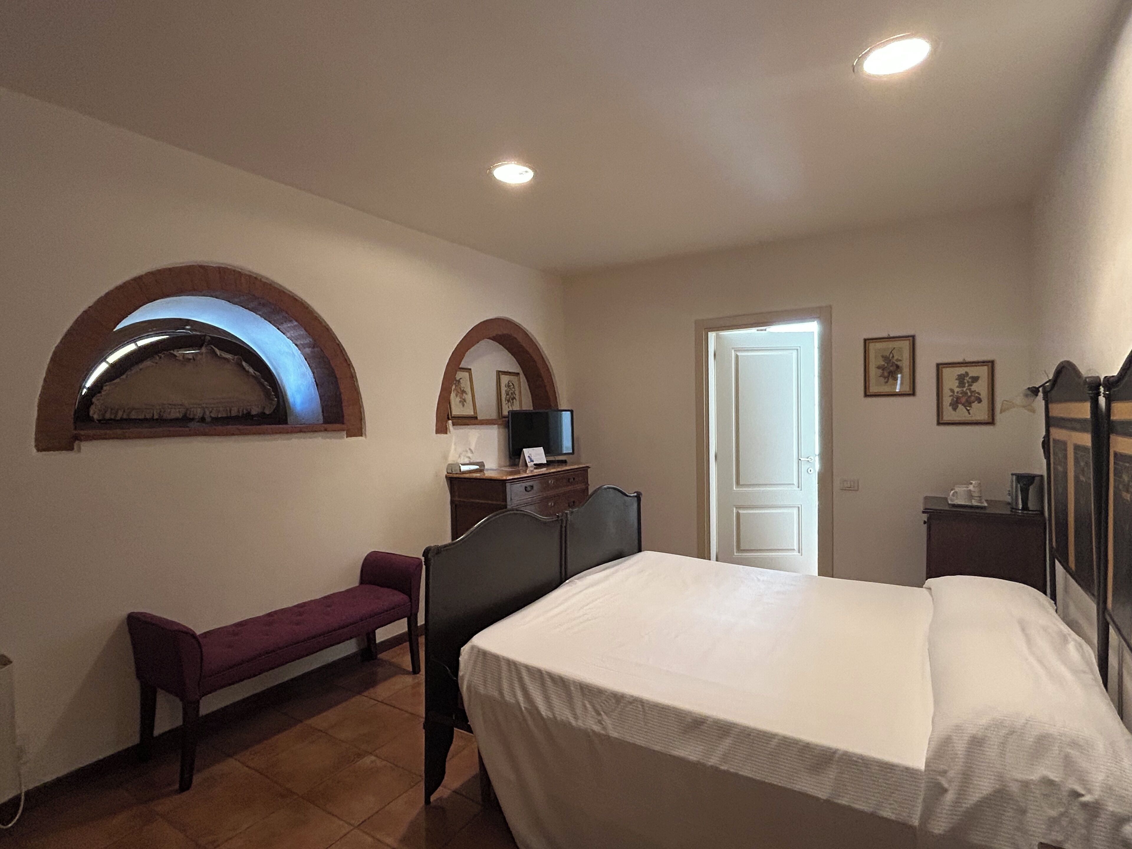 Un dormitorio con cama, una banca, un escritorio y una televisión, y una puerta.