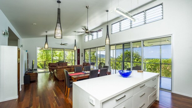 A spacious kitchen with a large island, modern pendant lights, and a view of greenery through large windows.