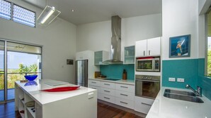 A modern kitchen with white cabinetry, a stainless steel refrigerator, a microwave, and a large window offering a view of greenery.