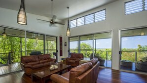 A spacious living area with leather sofas, a wooden coffee table, and large windows offering a view of greenery.