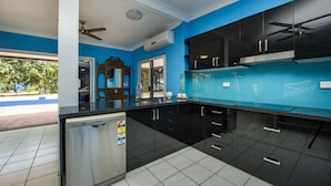 A modern kitchen with black cabinets, a stainless steel refrigerator, and a blue accent wall. - Azure on Geoffrey Bay (Arcadia)