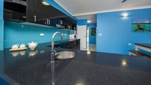 A modern kitchen with a black granite countertop, stainless steel faucet, and a microwave. There is a white door leading to another room. - Azure on Geoffrey Bay (Arcadia)