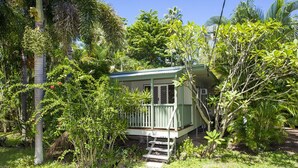 Ein kleines, eingeschossiges Haus mit Veranda, umgeben von üppiger Vegetation und Palmen.