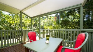 Eine überdachte Terrasse mit Tisch und zwei Stühlen, umgeben von einer Holzterrasse und üppiger Bepflanzung.