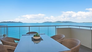Een balkon met een tafel en rieten stoelen, met uitzicht op een waterpartij en verafgelegen land.