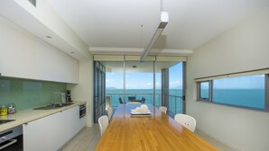 A modern kitchen with a wooden dining table, white chairs, and a view of the sea through large windows. - 1 Bright Point Apartment 4201 (Nelly Bay)