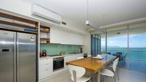 A modern kitchen with a built-in refrigerator, a dining area with a wooden table and white chairs, and a large window offering a view of the sea. - 1 Bright Point Apartment 4201 (Nelly Bay)