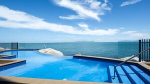 A swimming pool with clear blue water, a stone feature, and a view of the sea and mountains in the background. - 1 Bright Point Apartment 4201 (Nelly Bay)