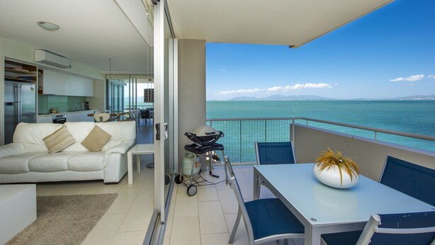 A modern living room with a sofa, a dining table with chairs, and a view of the sea. - 1 Bright Point Apartment 4201 (Nelly Bay)