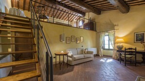 A spacious room with a wooden staircase, a sofa, a table, and a window with curtains. - Il Nido di Gabbiano (Scarperia e San Piero)