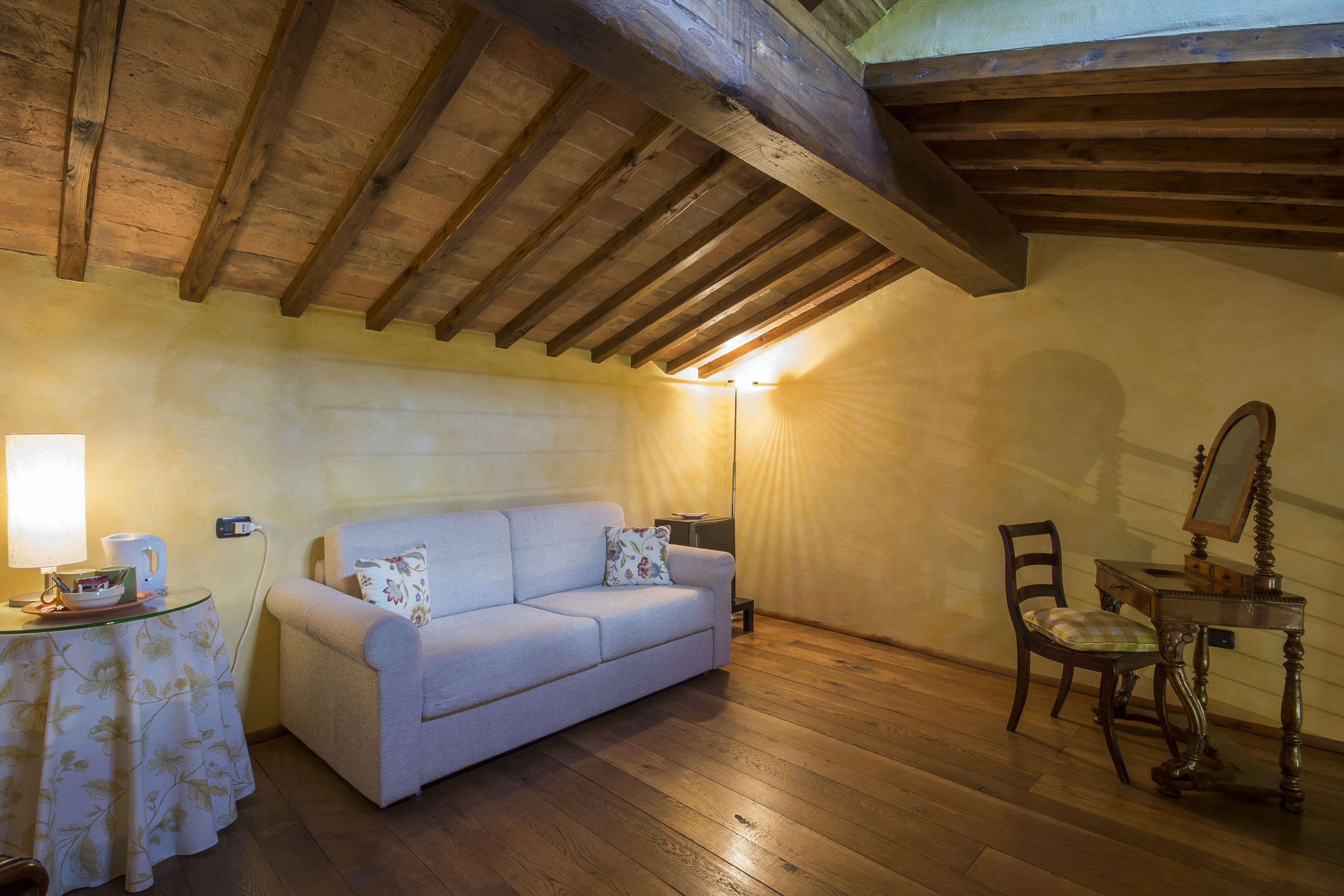 Una habitación acogedora con techo de madera, un sofá, una mesita con una lámpara y una silla.