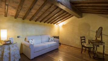 Una habitación acogedora con techo de madera, un sofá, una mesita con una lámpara y una silla.