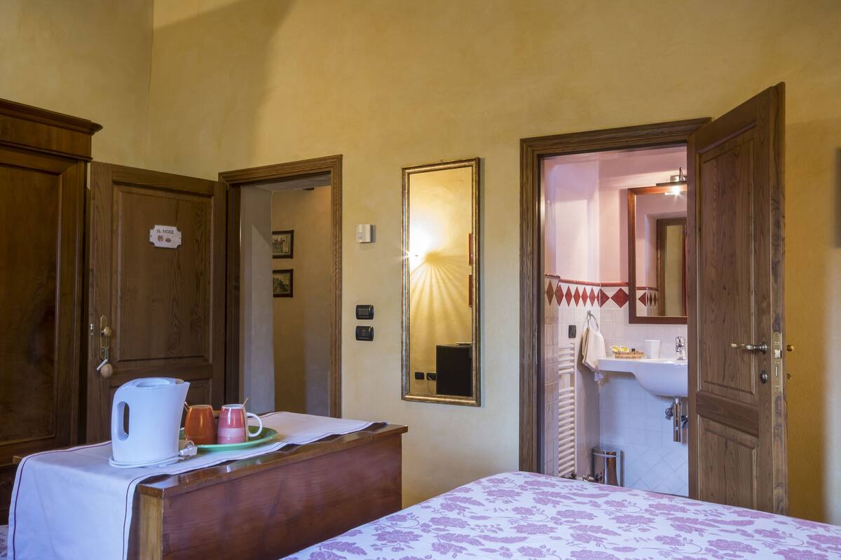 Una habitación de hotel con cama, cómoda de madera, espejo y baño visible a través de una puerta abierta.