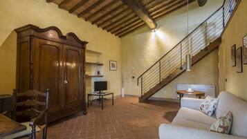 A spacious living area with a wooden cabinet, a sofa, a television on a stand, and a staircase.
